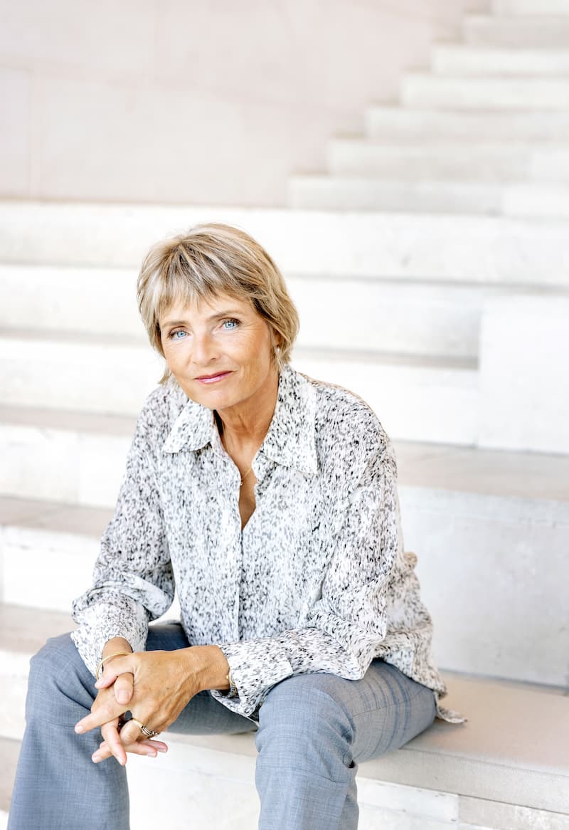 Portrætfoto, at Hanne-Vibeke Holst, der sidder på en trappe og hviler albuerne på sine knæ